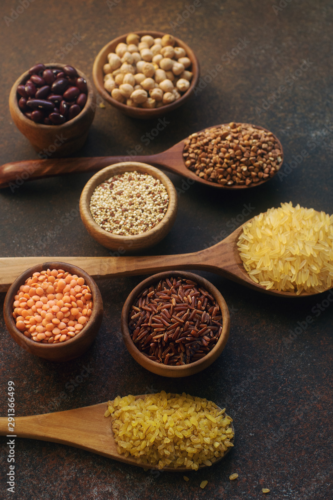 Various organic cereals and grains in wooden spoons and bowls on dark stone background Various organic cereals and grains in wooden spoons and bowls on dark stone background