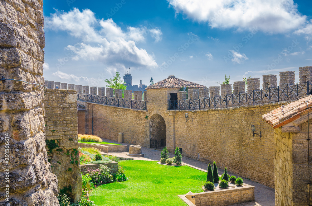 Obraz premium Stone brick fortress wall with merlons and courtyard of Prima Torre Guaita first tower and Seconda Torre La Cesta on Mount Titano rock with blue sky white clouds background in Republic San Marino