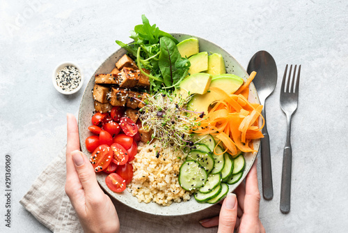Buddha bowl salad in female hands, balanced meal. Bright grey concrete background, table top view. Weight loss, dieting concept