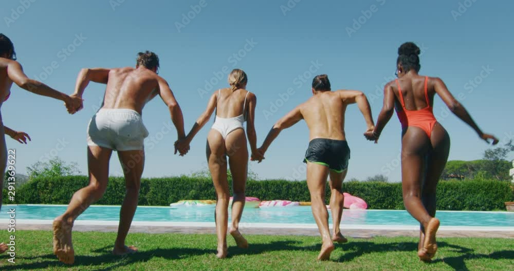 Authentic shot of young multi-ethnic friends in swimwear are having fun to enjoy their summer vacation together and jumping in a water in swimming pool in a sunny day.