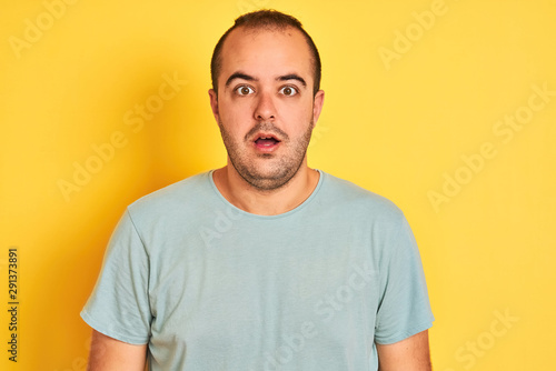 Young man wearing green casual t-shirt standing over isolated yellow background afraid and shocked with surprise expression, fear and excited face.