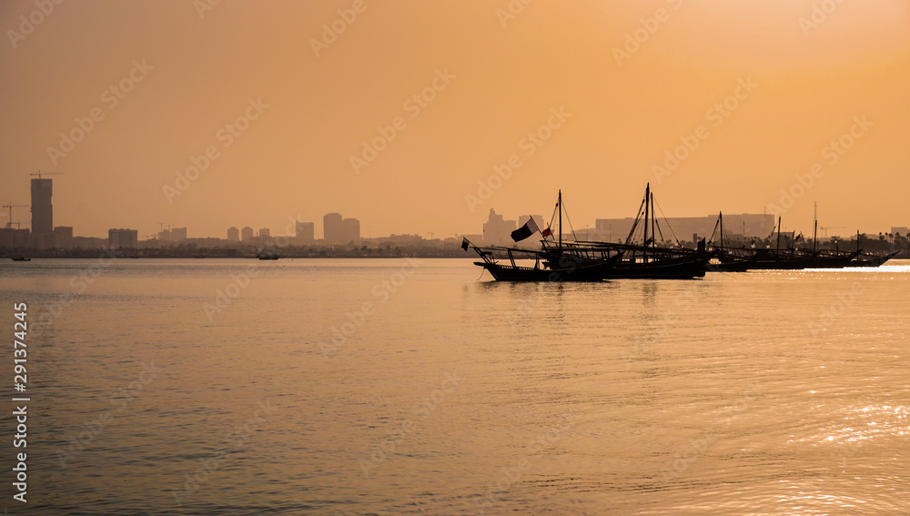 Traditional Arabic Dhow fishing boats in Doha bay during sunset as seen from Corniche waterfront promenade.