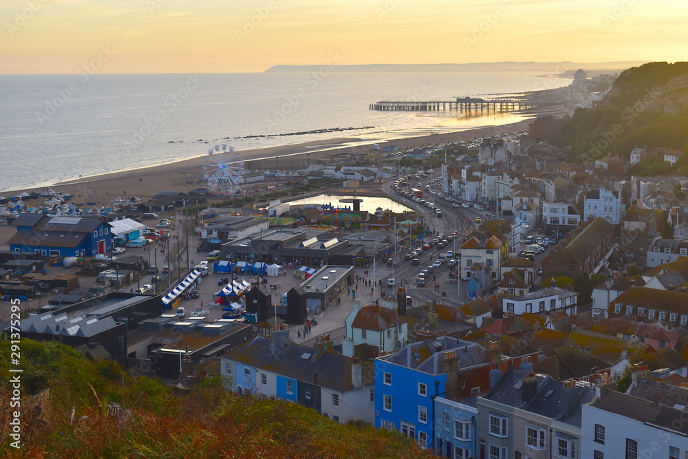 Aerial view of traditional English colourful seaside houses and warehouses. Sea meets romantic clear golden sunset sky. Hastings, Sussex, South East England