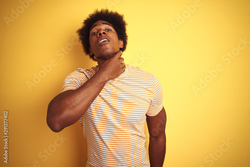 American man with afro hair wearing striped t-shirt standing over isolated yellow background Touching painful neck, sore throat for flu, clod and infection photo