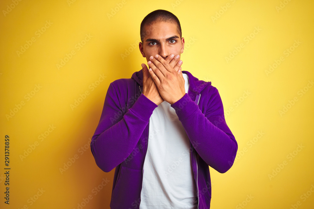 Young handsome man wearing purple sweatshirt over yellow isolated background shocked covering mouth with hands for mistake. Secret concept. Young handsome man wearing purple sweatshirt over yellow isolated background shocked covering mouth with hands for mistake. Secret concept.