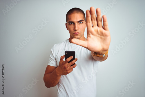 Young handsome man using smartphone over yellow isolated background with open hand doing stop sign with serious and confident expression, defense gesture