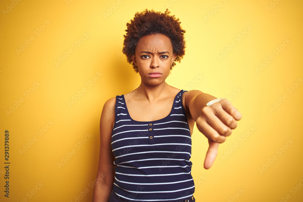 Beauitul african american woman wearing summer t-shirt over isolated yellow background looking unhappy and angry showing rejection and negative with thumbs down gesture. Bad expression. Beauitul african american woman wearing summer t-shirt over isolated yellow background looking unhappy and angry showing rejection and negative with thumbs down gesture. Bad expression.