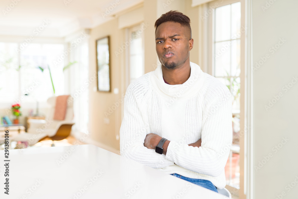 Handsome african american man on white table skeptic and nervous, disapproving expression on face with crossed arms. Negative person.