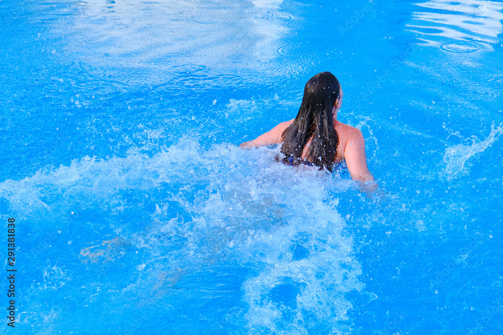 Young woman swims breaststroke in blue pool