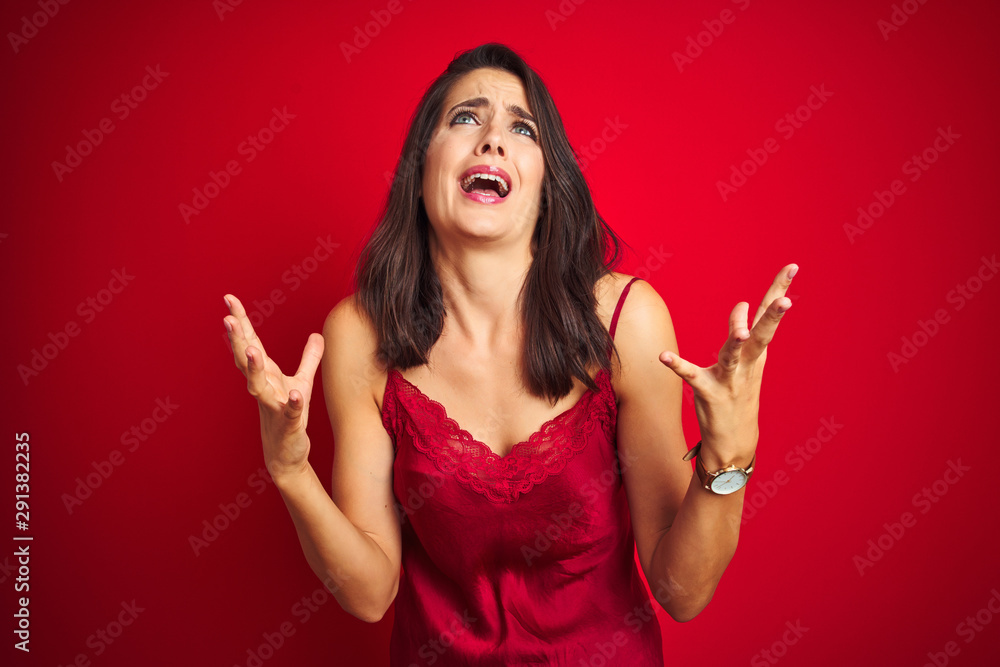 Young beautiful woman wearing sexy lingerie over red isolated background crazy and mad shouting and yelling with aggressive expression and arms raised. Frustration concept. Young beautiful woman wearing sexy lingerie over red isolated background crazy and mad shouting and yelling with aggressive expression and arms raised. Frustration concept.