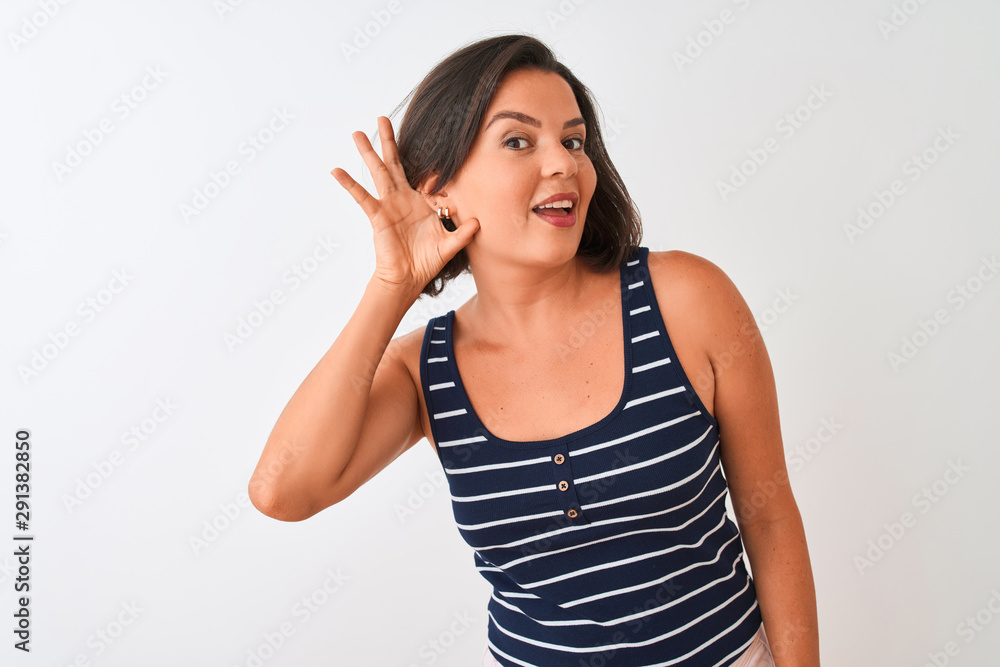Young beautiful woman wearing blue striped t-shirt standing over isolated white background smiling with hand over ear listening an hearing to rumor or gossip. Deafness concept. Young beautiful woman wearing blue striped t-shirt standing over isolated white background smiling with hand over ear listening an hearing to rumor or gossip. Deafness concept.