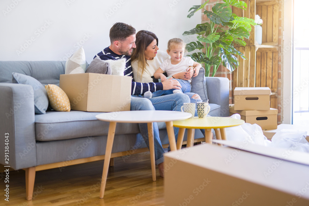 Beautiful family with kid sitting on the sofa drinking coffee at new home around cardboard boxes Beautiful family with kid sitting on the sofa drinking coffee at new home around cardboard boxes