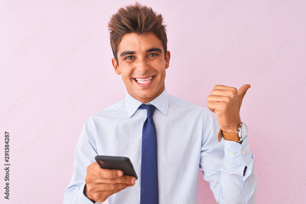 Young handsome businessman using smartphone standing over isolated pink background pointing and showing with thumb up to the side with happy face smiling Young handsome businessman using smartphone standing over isolated pink background pointing and showing with thumb up to the side with happy face smiling