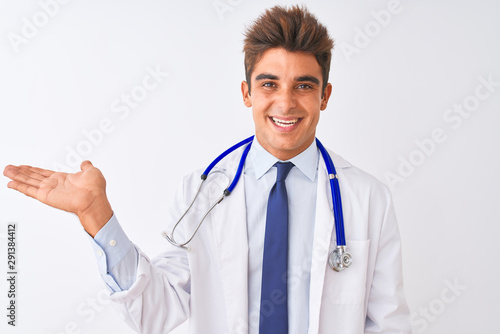 Young handsome doctor man wearing stethoscope over isolated white background smiling cheerful presenting and pointing with palm of hand looking at the camera.
