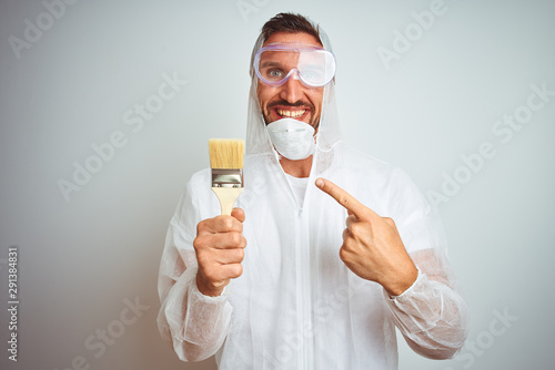 Painter man wearing professional worker equipment holding brush over isolated background very happy pointing with hand and finger