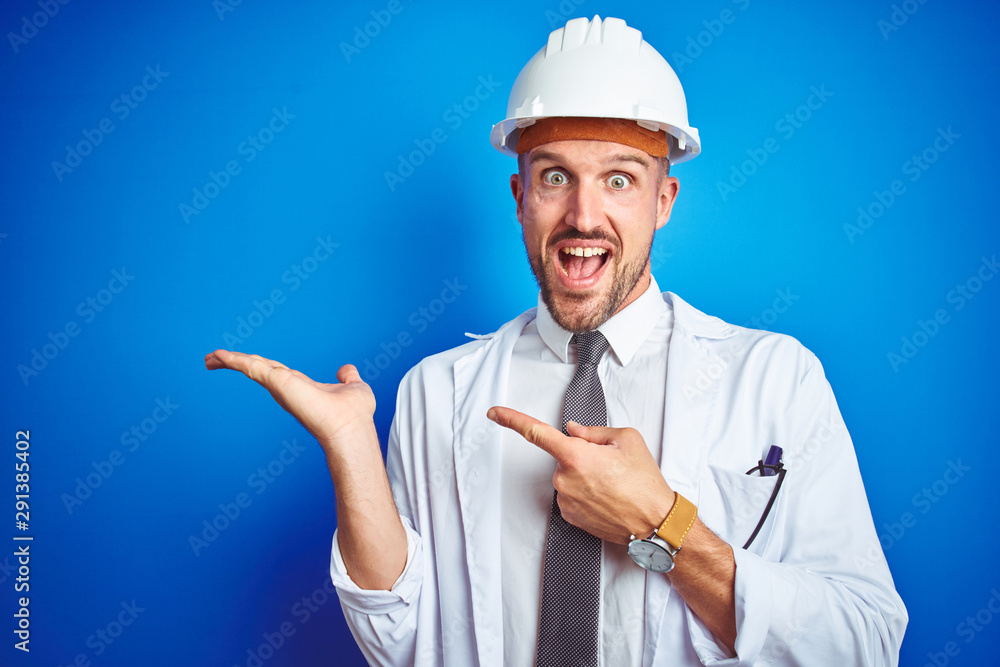 Young handsome engineer man wearing safety helmet over blue isolated background amazed and smiling to the camera while presenting with hand and pointing with finger. Young handsome engineer man wearing safety helmet over blue isolated background amazed and smiling to the camera while presenting with hand and pointing with finger.