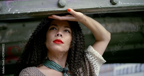 Close-up portrait of a bright beautiful brunette girl with curly hair, her red lips and nose piercing. She is under the bridge and posing with a handkerchief tied around her neck.