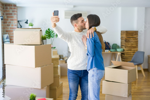 Beautiful couple taking a selfie photo using smartphone at new apartment, smiling happy for new house