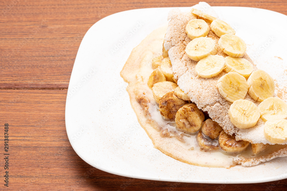 Tapioca filled with banana, cinnamon and condensed milk, on wooden background. Flatbread made from cassava (also known as casabe, bammy, beiju, bob, biju). Tapioca filled with banana, cinnamon and condensed milk, on wooden background. Flatbread made from cassava (also known as casabe, bammy, beiju, bob, biju).