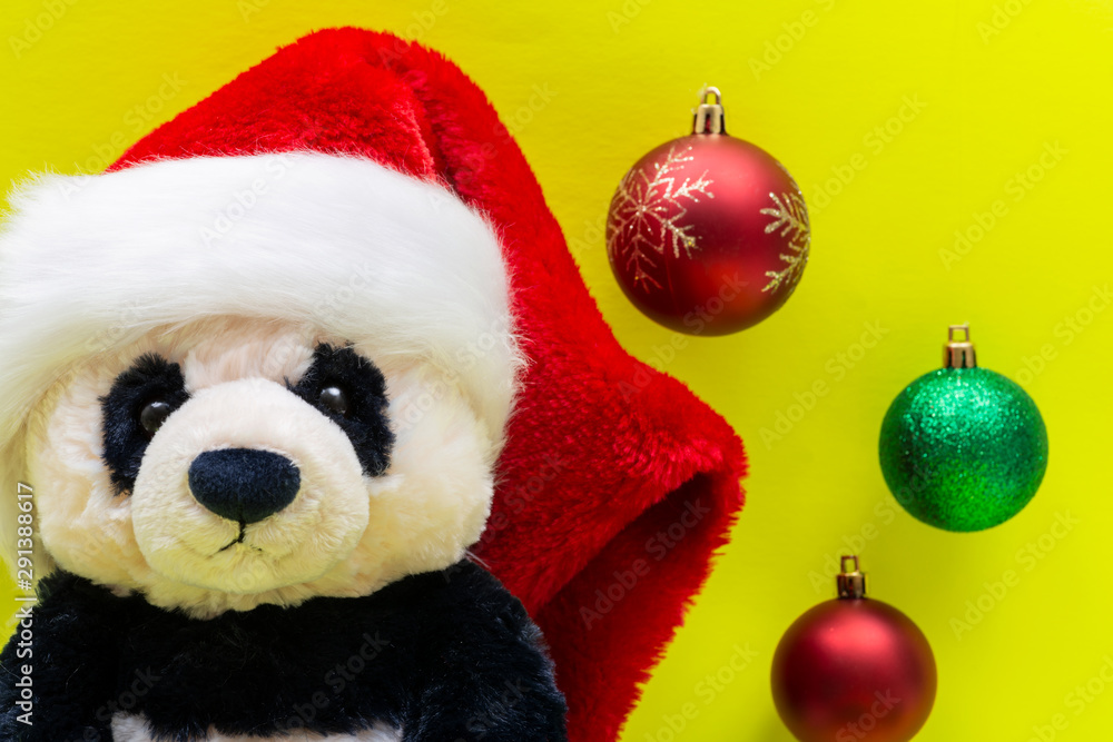 Panda Bear plush toy with Red Christmas Santa Hat surrounded by Colorful Vintage Ornaments on bright yellow background. Winter Holidays concept.