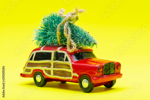 Christmas Tree on a toy car on bright yellow background. Winter Holidays celebration concept.