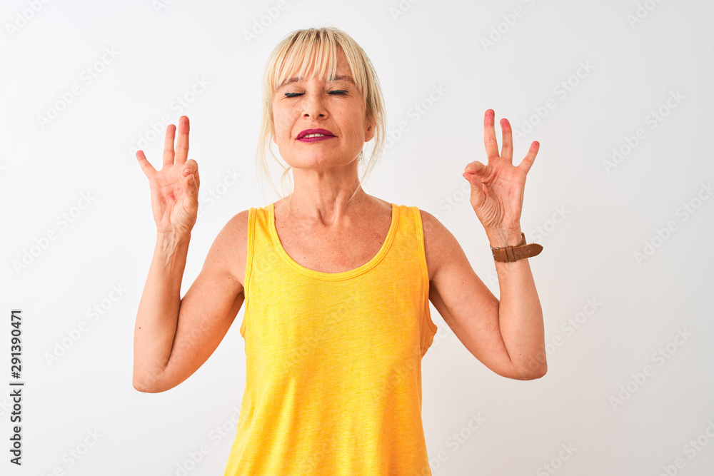Middle age woman wearing yellow casual t-shirt standing over isolated white background relax and smiling with eyes closed doing meditation gesture with fingers. Yoga concept.