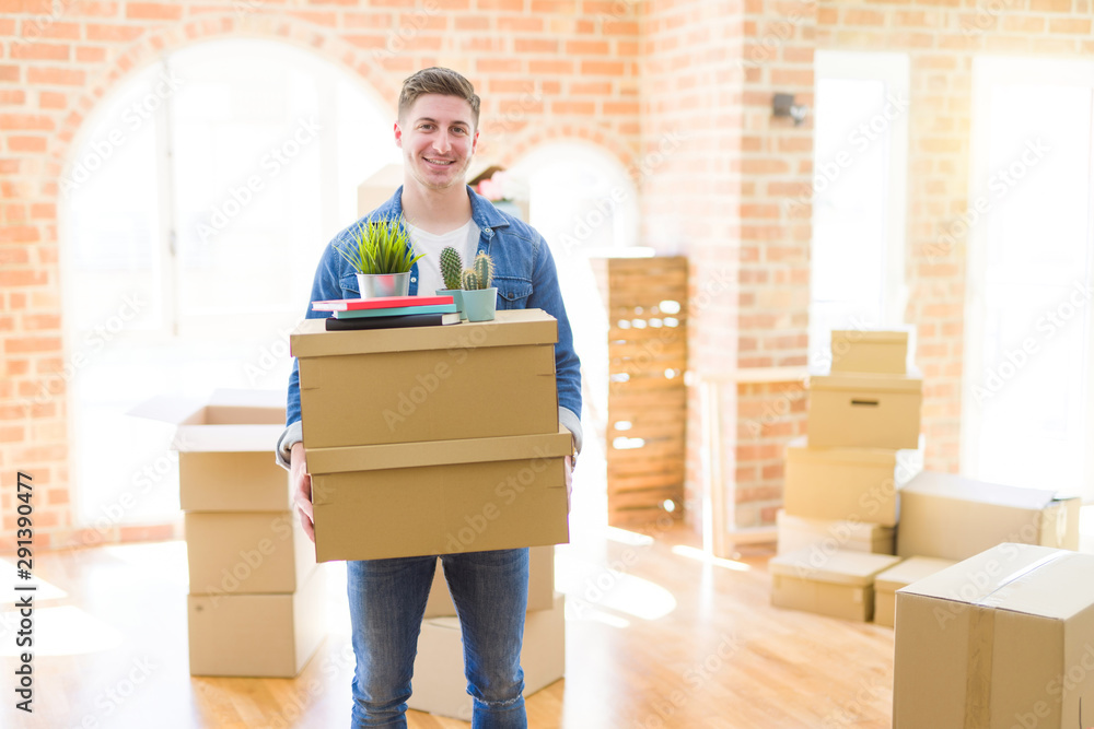 Handsome young man smiling happy moving to a new home, very excited holding cardboard boxes at new apartment Handsome young man smiling happy moving to a new home, very excited holding cardboard boxes at new apartment