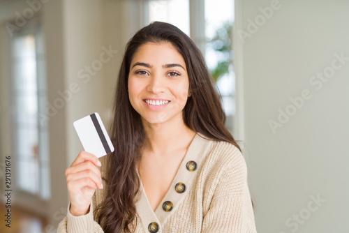 Young woman holding credit card as payment with a happy face standing and smiling with a confident smile showing teeth