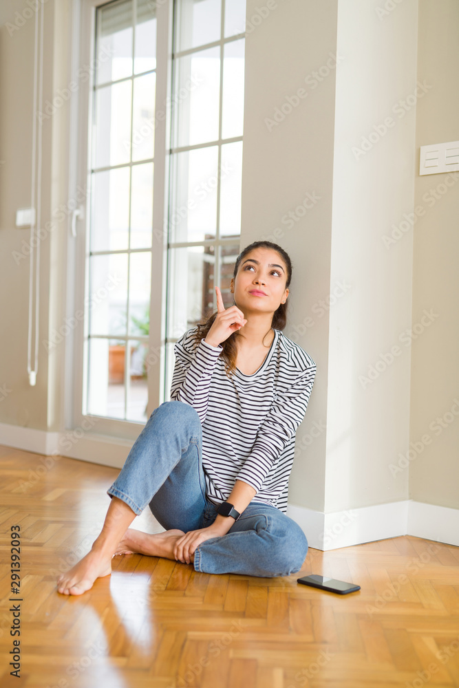 Beautiful young woman smiling cheerful pointing to the side with fingers sitting on the floor Beautiful young woman smiling cheerful pointing to the side with fingers sitting on the floor