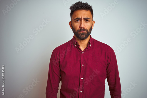 Young indian man wearing red elegant shirt standing over isolated grey background depressed and worry for distress, crying angry and afraid. Sad expression.