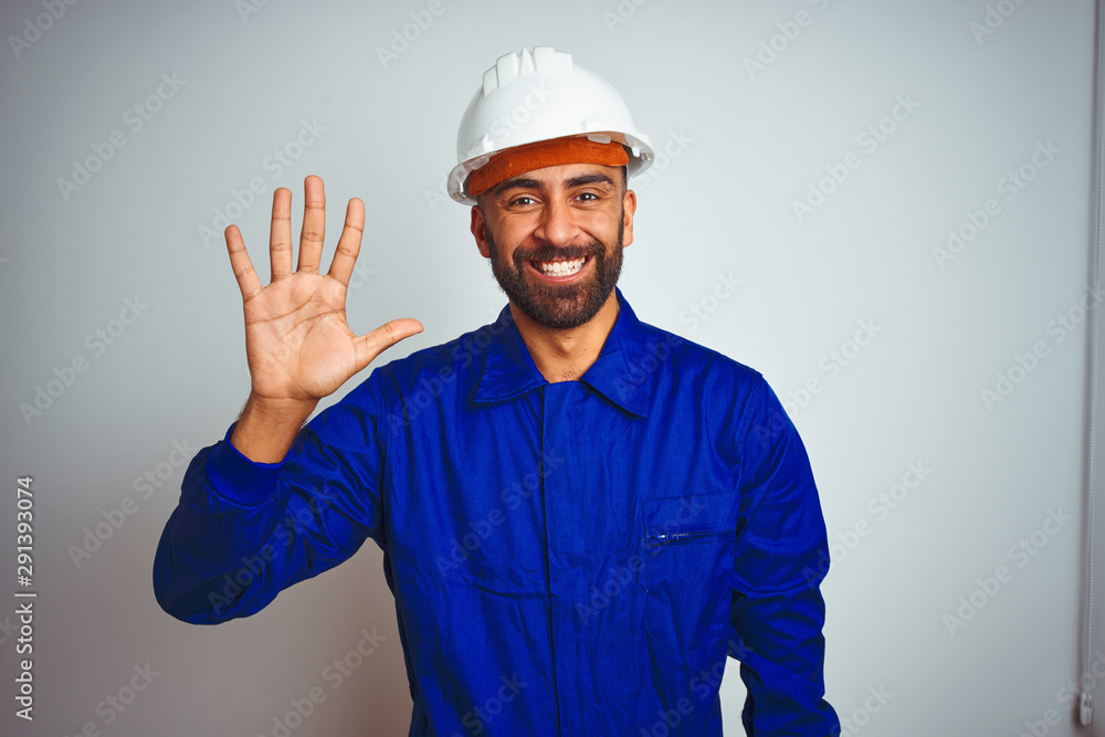 Handsome indian worker man wearing uniform and helmet over isolated white background showing and pointing up with fingers number five while smiling confident and happy.