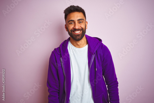Young indian man wearing purple sweatshirt standing over isolated pink background with a happy and cool smile on face. Lucky person.