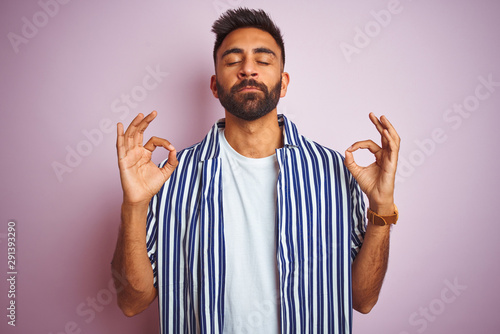 Young handsome indian man wearing summer striped shirt over isolated pink background relax and smiling with eyes closed doing meditation gesture with fingers. Yoga concept.