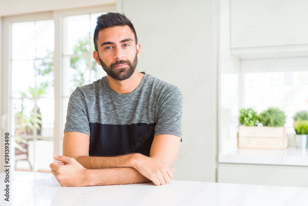 Fototapeta premium Handsome hispanic man wearing casual t-shirt at home with serious expression on face. Simple and natural looking at the camera.