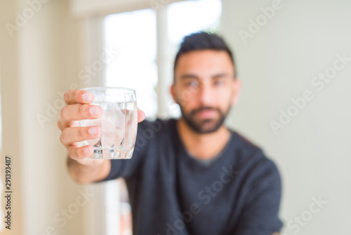 Handsome hispanic man drinking a fresh glass of water with a confident expression on smart face thinking serious