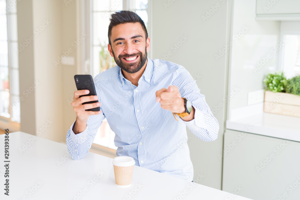 Handsome hispanic business man drinking coffee and using smartphone pointing with finger to the camera and to you, hand sign, positive and confident gesture from the front
