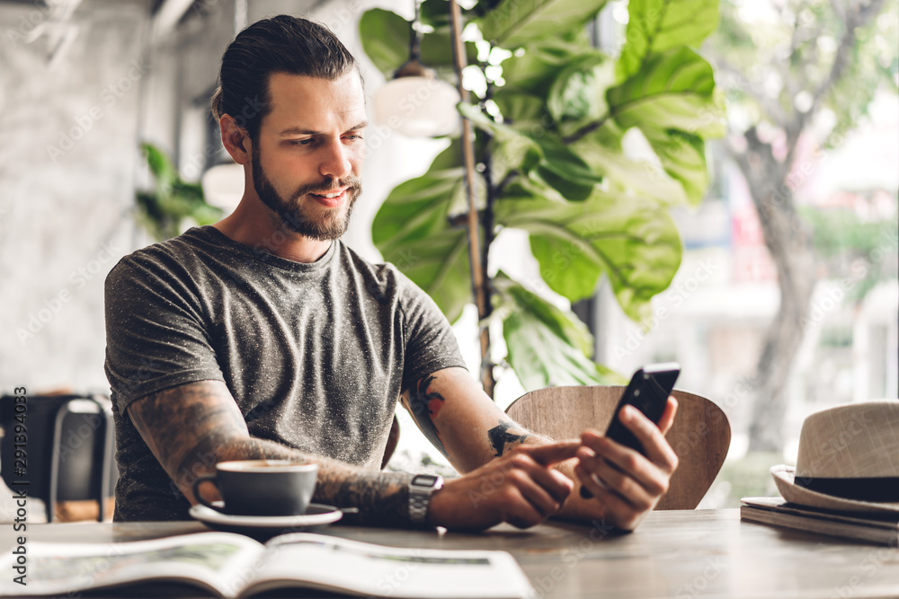 Handsome bearded hipster man use smartphone with coffee at table in cafe.Communication and technology concept Handsome bearded hipster man use smartphone with coffee at table in cafe.Communication and technology concept