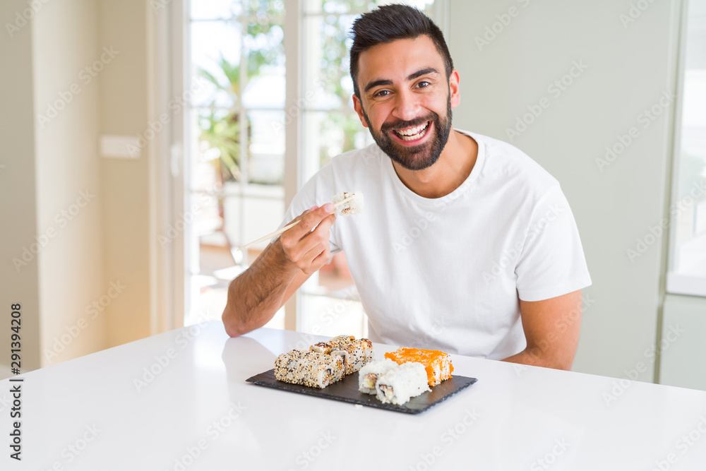 Handsome man smiling happy enjoying eating fresh colorful asian sushi using chopsticks Handsome man smiling happy enjoying eating fresh colorful asian sushi using chopsticks
