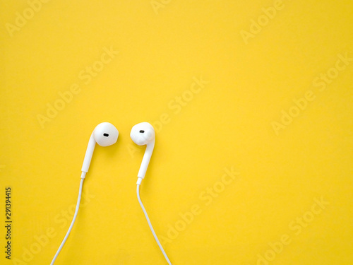 White earphones on yellow background. Earphones for listening to music and sound on portable devices.