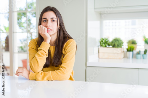 Beautiful young woman wearing yellow sweater looking stressed and nervous with hands on mouth biting nails. Anxiety problem.