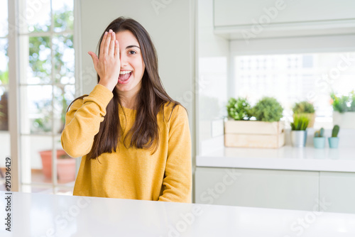 Beautiful young woman wearing yellow sweater covering one eye with hand with confident smile on face and surprise emotion. Free Download Beautiful young woman wearing yellow sweater covering one eye with hand with confident smile on face and surprise emotion. - GFXLoad