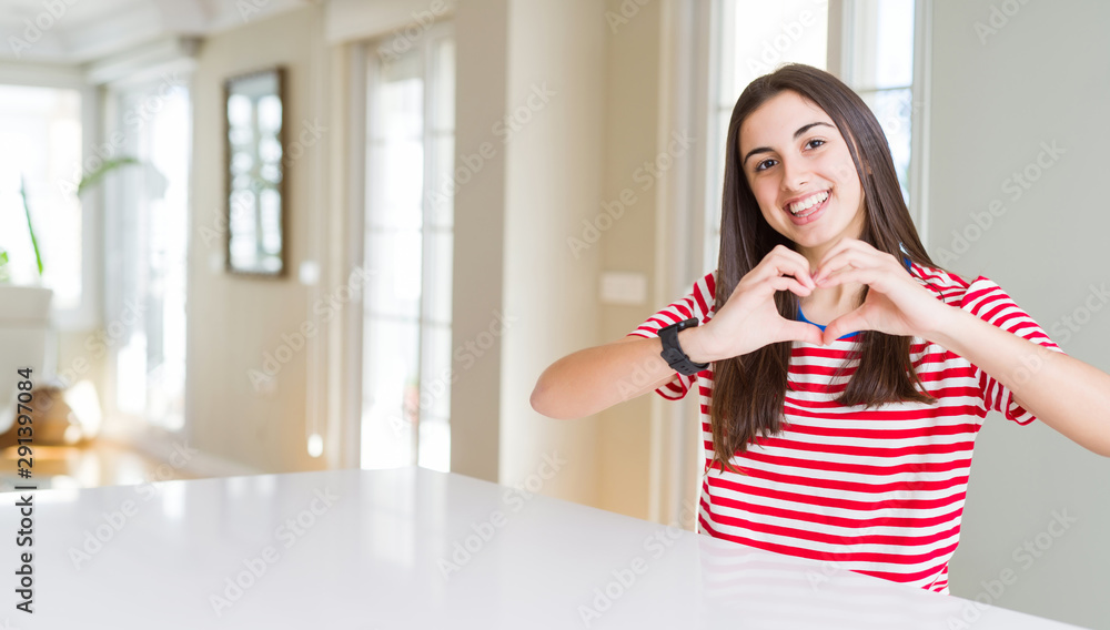Beautiful young woman wearing casual stripes t-shirt smiling in love showing heart symbol and shape with hands. Romantic concept. Beautiful young woman wearing casual stripes t-shirt smiling in love showing heart symbol and shape with hands. Romantic concept.