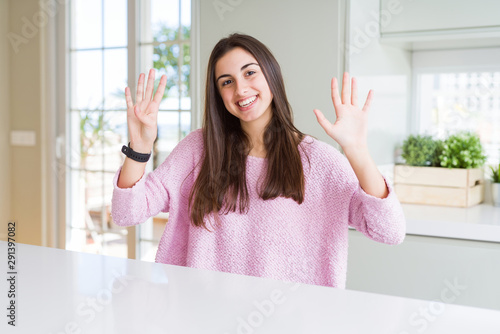 Beautiful young woman wearing pink sweater showing and pointing up with fingers number nine while smiling confident and happy.
