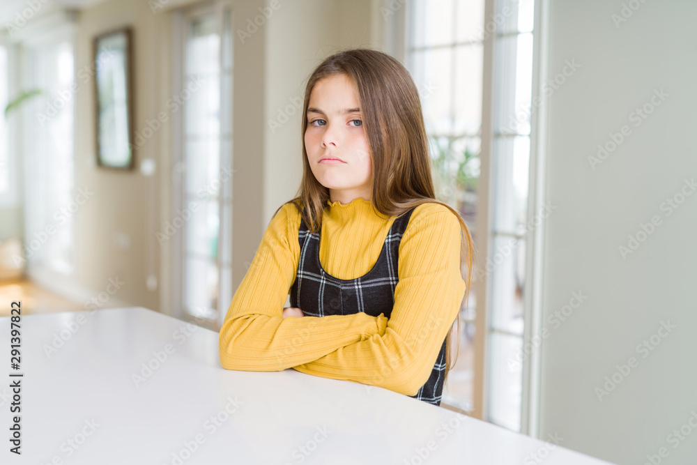 Beautiful young girl kid sitting on the table skeptic and nervous, disapproving expression on face with crossed arms. Negative person.