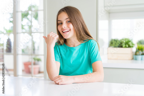 Beautiful young girl kid wearing green t-shirt smiling with happy face looking and pointing to the side with thumb up.