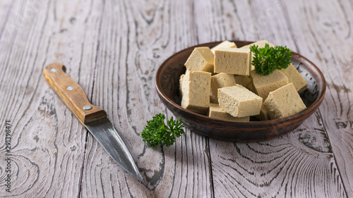 Pieces of tofu cheese in a clay bowl and a knife on a wooden table. Soy cheese.