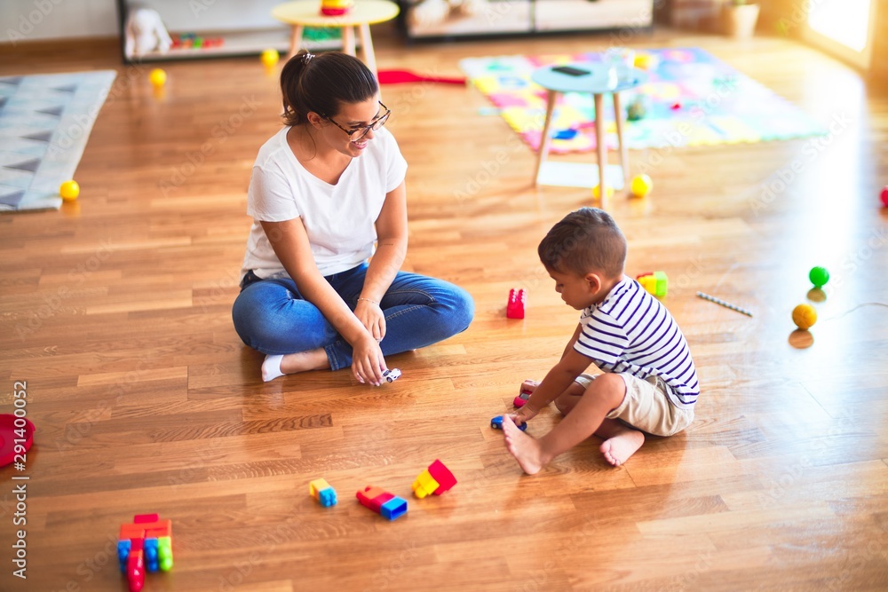 Fototapeta premium Beautiful teacher and toddler boy playing with tractor and cars at kindergarten