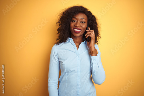 Young african american woman talking on the smartphone over isolated yellow background with a happy face standing and smiling with a confident smile showing teeth