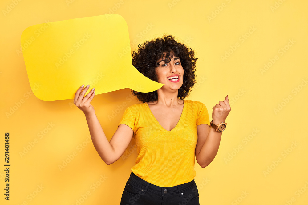 Young arab woman with curly hair holding speech bubble over isolated yellow background screaming proud and celebrating victory and success very excited, cheering emotion Young arab woman with curly hair holding speech bubble over isolated yellow background screaming proud and celebrating victory and success very excited, cheering emotion