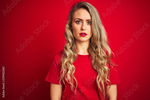 Young beautiful woman wearing basic t-shirt standing over red isolated background Relaxed with serious expression on face. Simple and natural looking at the camera.